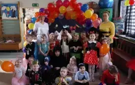 grupa dzieci i panie nauczycielki w karnawałowych przebraniach poują do zdjęcia na tle łuku z balonami