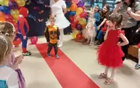 chłopiec w przebraniu dyni na czerwonym dywanie dookoła inne dzieci i pani nauczycielka z mikrofonem