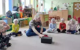 dzieci siedzą w kole pan między nimi coś pokazuje