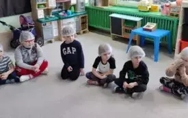 dzieci siedzą na dywanie na głowach mają czepki ochronne