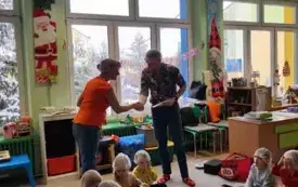 nauczycielka podaje rękę panu, dzieci siedzą na podłodze wszyscy w czepkach ochronnych