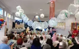 grupa dzieci w przebraniach w tle dekoracja na g&oacute;rze zawieszone białe balony przed dziećmi starsze osoby