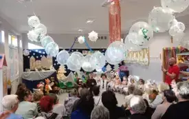 grupa dzieci w przebraniach w tle dekoracja na g&oacute;rze zawieszone białe balony przed dziećmi starsze osoby