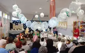 grupa dzieci w przebraniach w tle dekoracja na g&oacute;rze zawieszone białe balony przed dziećmi starsze osoby