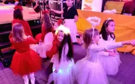 dziewczynki w białych i czerwonych sukienkach stoją przed wejściem na scenę widać banery Wielkiej orkiestri świątecznej pomocy z nimi pani Monika