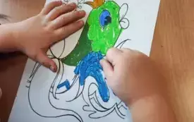 ręce dziecka na stole kolorujące obrazek ryby w koronie