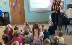 dzieci siedzą na dywanie przed nimi tablica multimedialna obok pani 