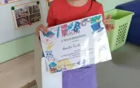 dziewczynka pozuje do zdjęcia z dyplomem konkursowym
