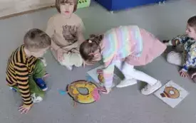 dzieci siedzą na dywanie przed nimi obrazki donat&oacute;w oraz udonaty ułożone z element&oacute;w