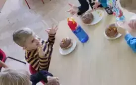 dzieci przy stolikach jedzą pączki