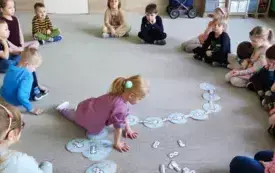 dzieci siedzą w kole na dywanie dziewczynka układa domino na środku dywanu