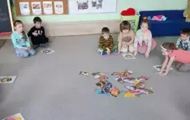 dzieci siedzą na dywanie przed nimi obrazki z pączkami  na środku dywanu pocięte sylwety poączk&oacute;w