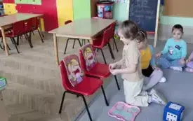 dwa krzesełka na nich sylwetki dzieci, chłopiec wkłada do otworu jednej s sylwetek papierowego donata