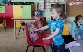 dwa krzesełka na nich sylwetki dzieci, chłopiec wkłada do otworu jednej s sylwetek papierowego donata