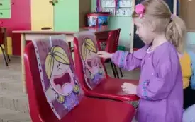 dwa krzesełka na nich sylwetki dzieci, dziewczynka wkłada do otworu jednej s sylwetek papierowego donata
