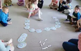 dzieci siedzą w kole na dywanie dziwczynka układa domino 