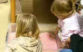 dwoje dzieci kuca przy dużym pojemniku z kolorowym ryżem