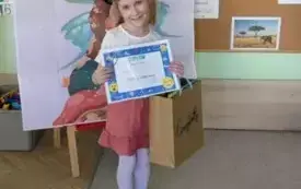 dziewczynka trzyma dyplom i torebkę prezentową pozuje do zdjęcia