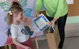nauczycielka podaje dyplom i torebkę papierową dziewczynce