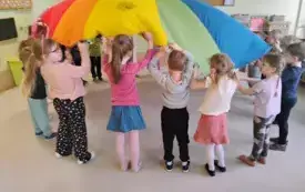 dzieci trzymają w g&oacute;rze chustę animacyjną napompowaną jak balon