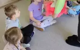 dzieci siedzą w kole nauczycielka nachyla się nad nimi z pudełkiem udekorowanym r&oacute;żowym tiulem