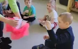 dzieci siedzą w kole nauczycielka nachyla się nad nimi z pudełkiem udekorowanym r&oacute;żowym tiulem