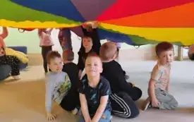 dzieci siedzą pod kolorową chustą animacyjną