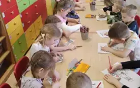 dzieci siedzą przy jednym długim stole i kolorują laurki