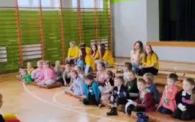 sala gimnastyczna szkolna dzieci siedzą na matach sportowych 