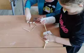 dzieci stoją przy stoliku w rękach trzymają imitacje wykopalisk na stoliku leżą małe drewniane narzędzia młoteczki