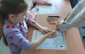 dzieci siedzą przy stole przed nimi kolorowanki kredki i flamastry