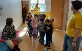 grupa dzieci na korytarzu w szkole z nimi dwoje uczni&oacute;w w ż&oacute;łtych koszulkach na podłodze naklejki kolorowych st&oacute;p