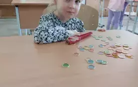 dziewczynka przy stoliku z małymi kolorowymi krążkami