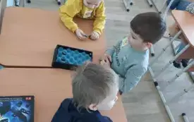 trzech chłopc&oacute;w przy stoliku na kt&oacute;rym leży pudełko z magnesami