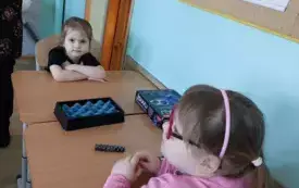 dwie dziewczynki siedzą przy stoliku na kt&oacute;rym leży pudełko z magnesami