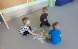 tr&oacute;jka dzieci na dywanie przed nimi układanak a z motywem skarpetek