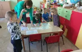 dzieci i nauczyciel przy stoliku przed nimi karty pracy ze wzorem i motywem skarpetek