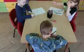 tr&oacute;jka dzieci przy stoliku przed nimi karty pracy z motywem skarpetek