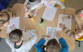 dzieci siedza przy stoliku, kolorują karty pracy z wzorami skarpetek
