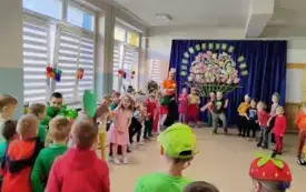 dzieci i nauczycielka w kolorowych owocowo warzywnych strojach stoją w kole w tle dekoracja kosz z owocami i warzywami