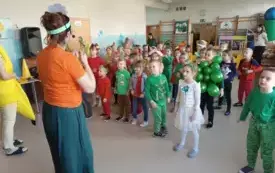 nauczycielka z mikroportem stoi przed grupą dzieci w kolorowych owocowo warzywnych przebraniach