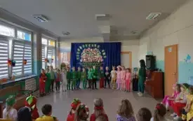 grupa dzieci w kolorowych ubraniach stoi w p&oacute;łkolu obok nauczycielka ubrana na zielono