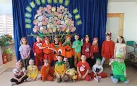 grupa dzieci w przebraniach owocowo-warzywnych pozuje na tle dekoracji kosz z owocami i warzywami