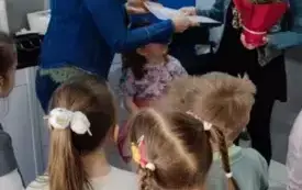 pani fryzjerka trzyma kwiat w doniczce, pani nauczycielka wręcza jej kartkę dookoła dzieci