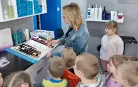 pani fryzjerka stoi przed paletą z kolorami włos&oacute;w dzieci przyglądają się