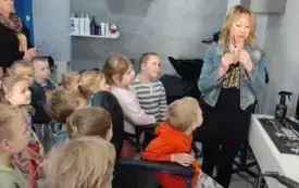 wnętrze salonu fryzjerskiego dzieci przyglądaja sie pani fryzjerce kt&oacute;ra trzyma małe nożyczki