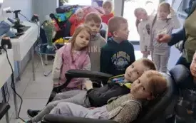 wnętrze salonu fryzjerskiego z jego atrybutami dwoje dzieci siedzi na fotelu reszta dzieci stoi dookoła