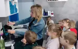pani fryzjerka pokazuje dzieciom czarną miseczkę z pędzelkiem dzieci przyglądają się