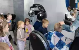 chłopiec siedzi na fotelu pani fryzjerka robi mu fryzurę dzieci przyglądają się