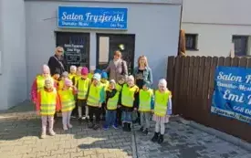 Dzieci stoją przed salonem fryzjerskim z nimi trzy panie dzieci maja na sobie odblaskowe kamizelki